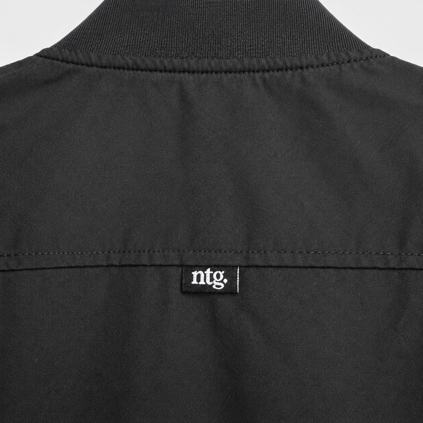 Close-up of the ribbed back collar and small ntg. label on a black NTG bomber jacket.