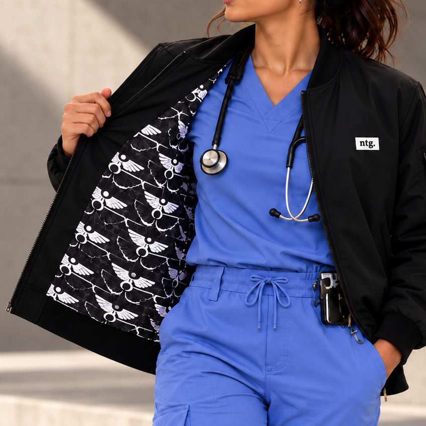Model in blue scrubs holding open a black Arterial bomber jacket to show its black-and-white monogram lining.