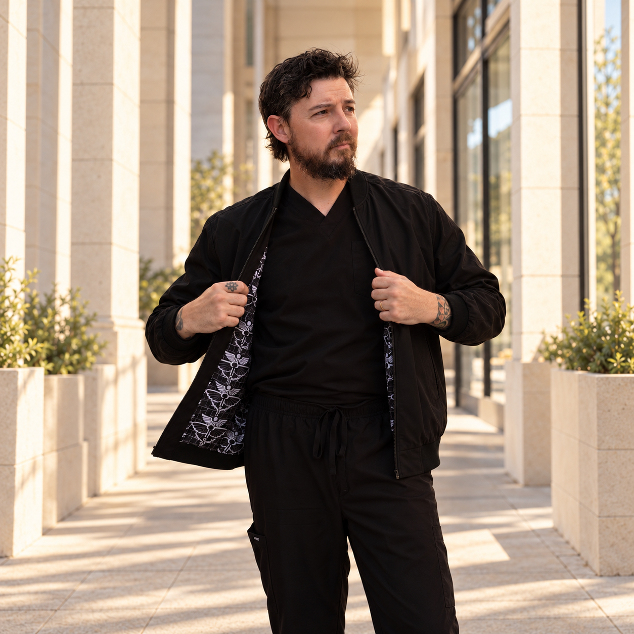 Model in black scrubs holding open an Arterial bomber jacket to show its monogram lining.