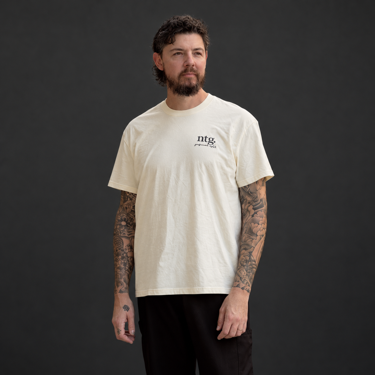 Front view of a model wearing a cream Sure’t T-shirt with a small ntg. chest print.