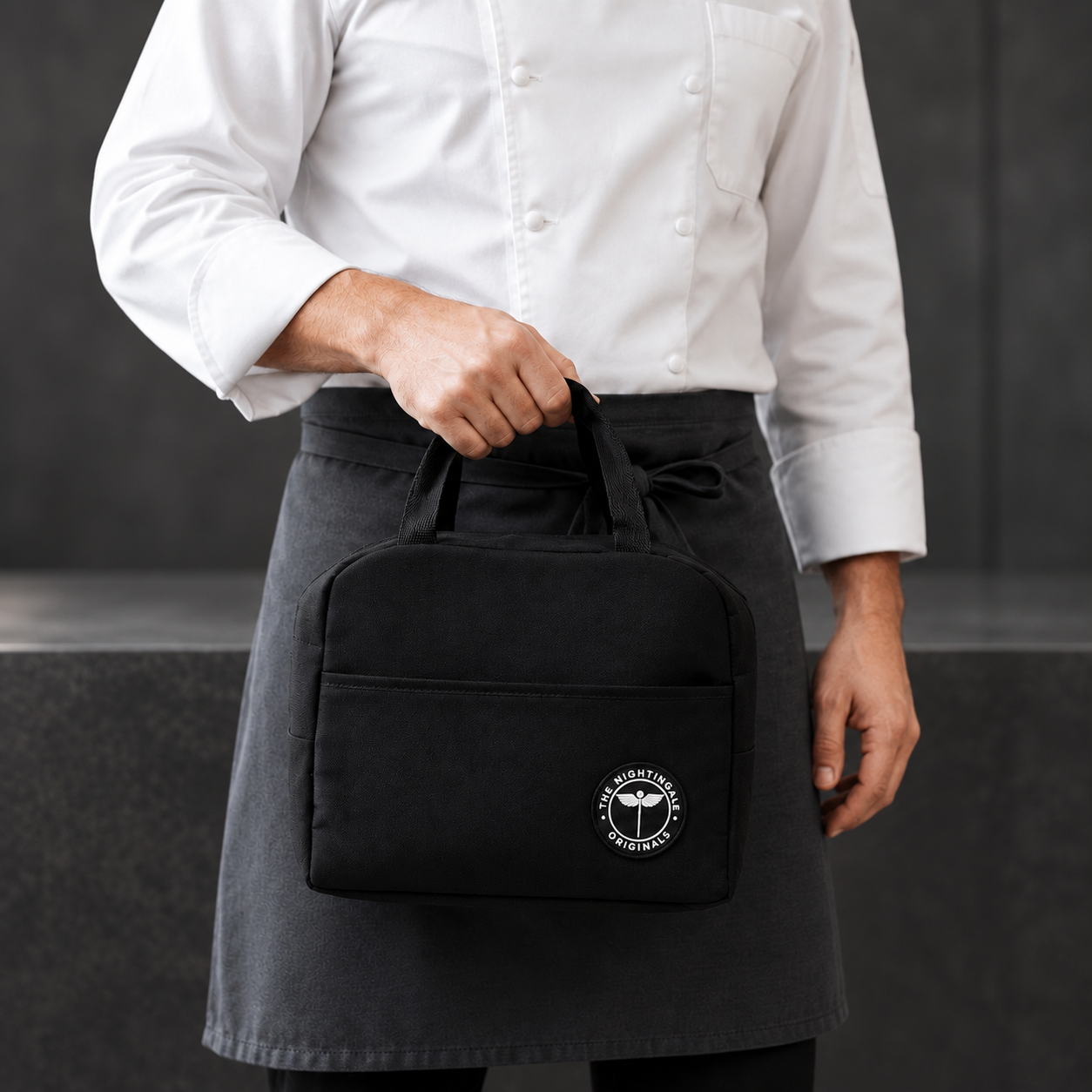 Person in a white shirt carrying a black Famish’d lunch tote by its handles.