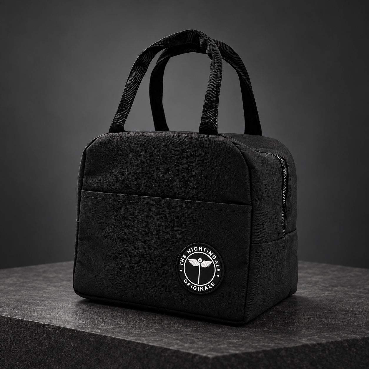 Black Famish’d insulated lunch tote with two handles, a front pocket and circular NTG emblem on a dark display.