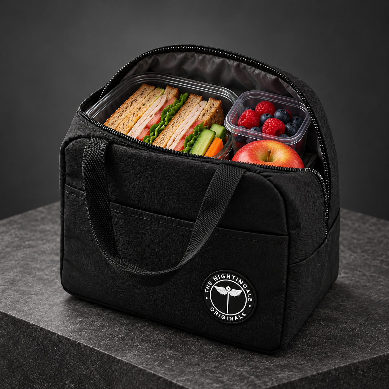 Open black Famish’d lunch tote packed with sandwiches, fruit and food containers.
