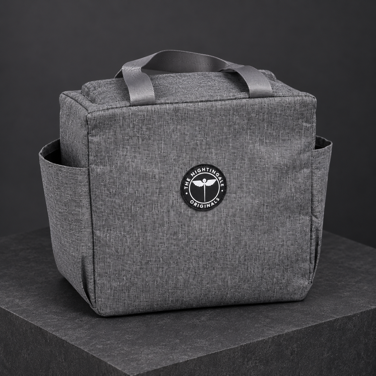 Three-quarter view of a gray Famish’d lunch bag showing the handles, front pocket and side panel.
