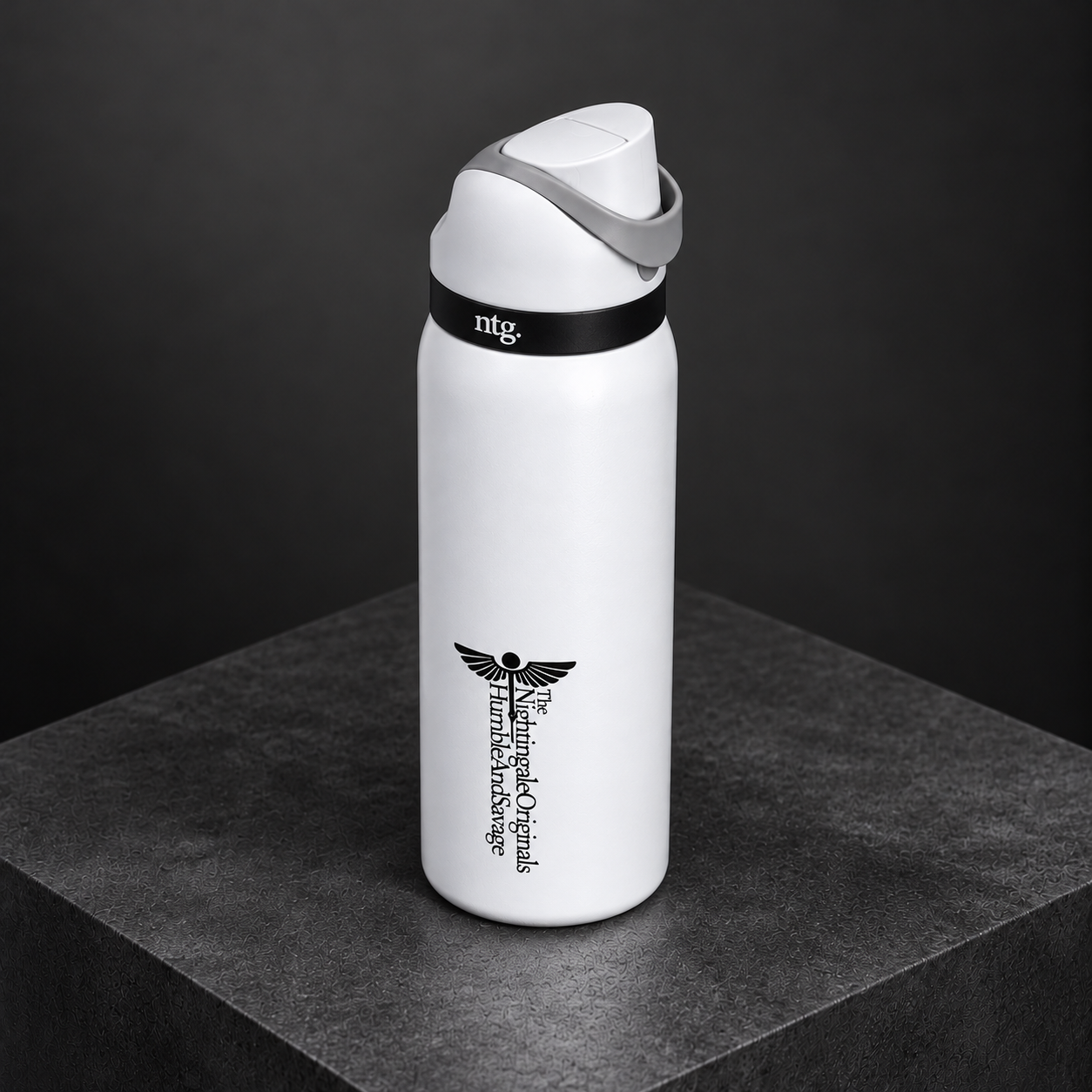 Elevated view of a white Parch’d tumbler, gray lid and black collar on a charcoal plinth.