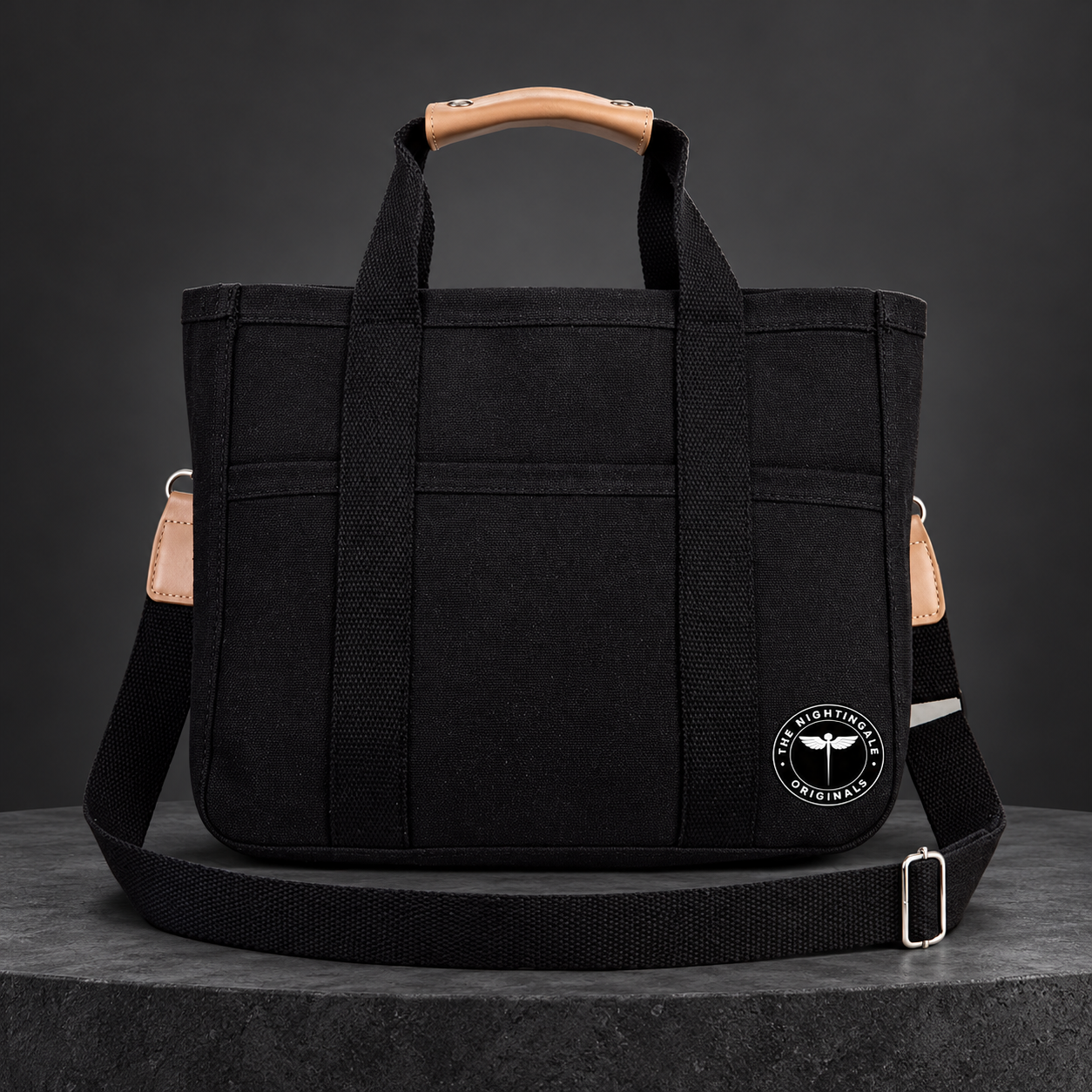 Black Satch’l clinical tote with tan handles, shoulder strap, front pockets and round NTG emblem.