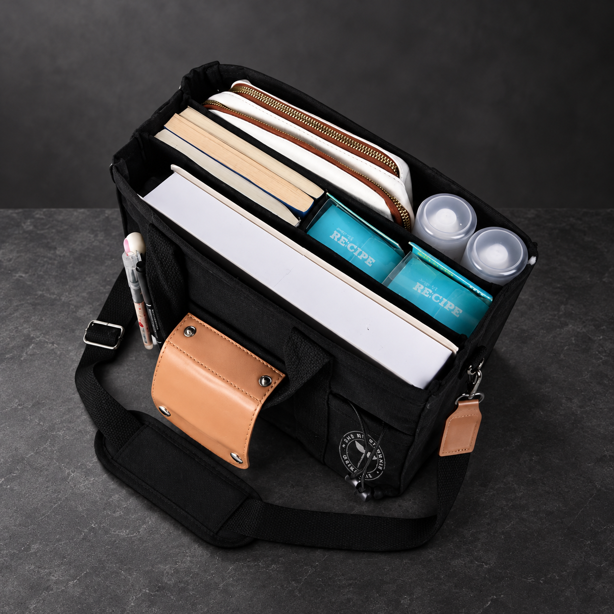 Overhead view into a black Satch’l clinical tote holding notebooks, a phone and bottles in organizer pockets.