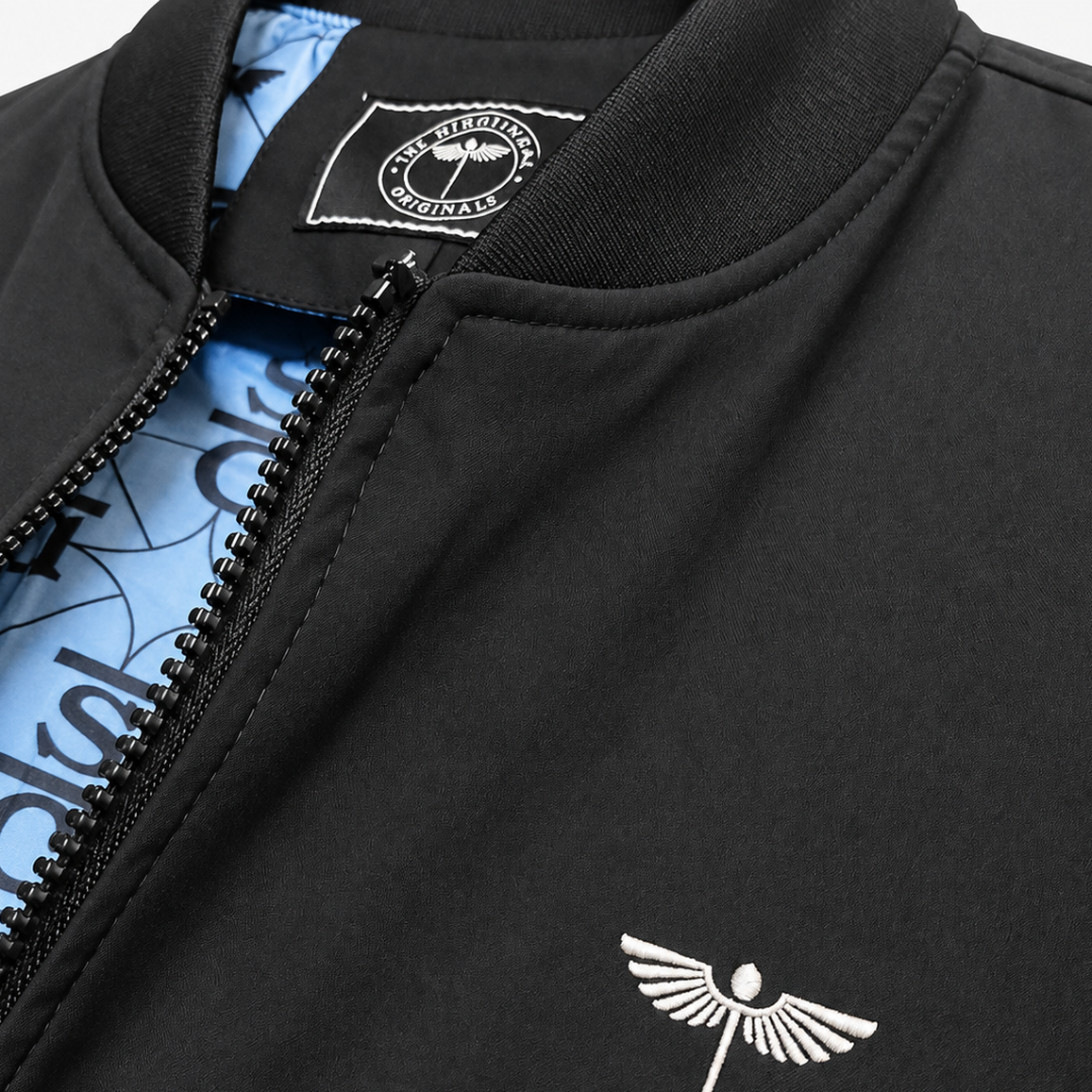 Close-up of a black Venous bomber jacket showing its chest emblem, zipper, neck label and blue lining.