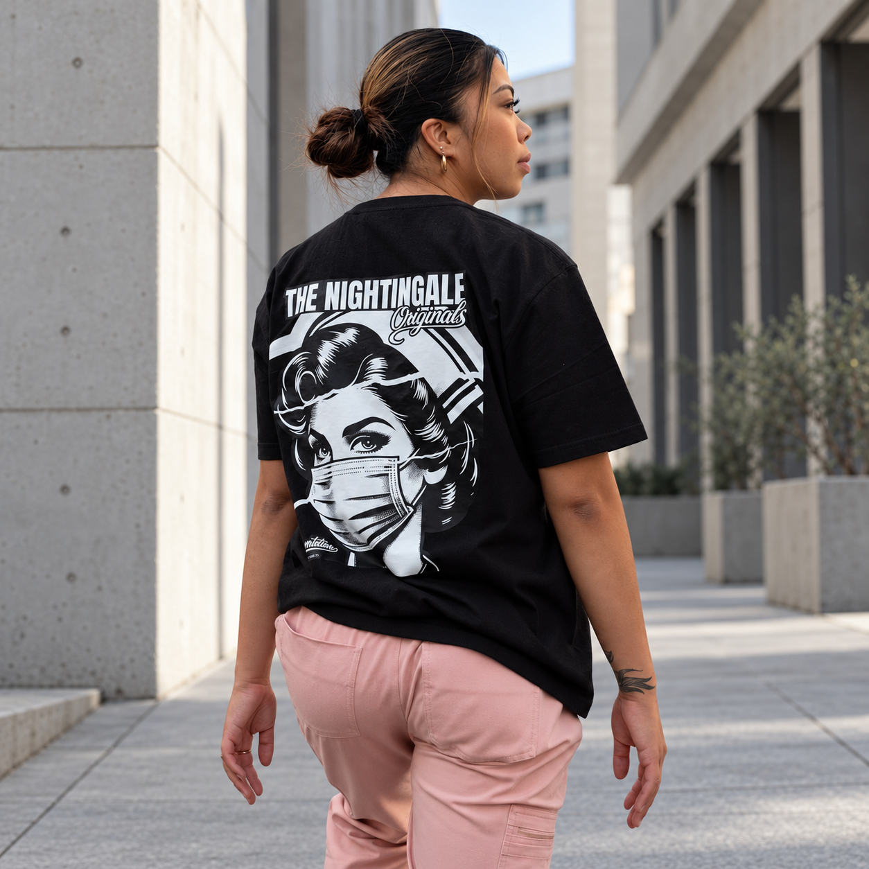 Model in pink trousers wearing a black Sure’t T-shirt with a large masked-nurse graphic on the back.