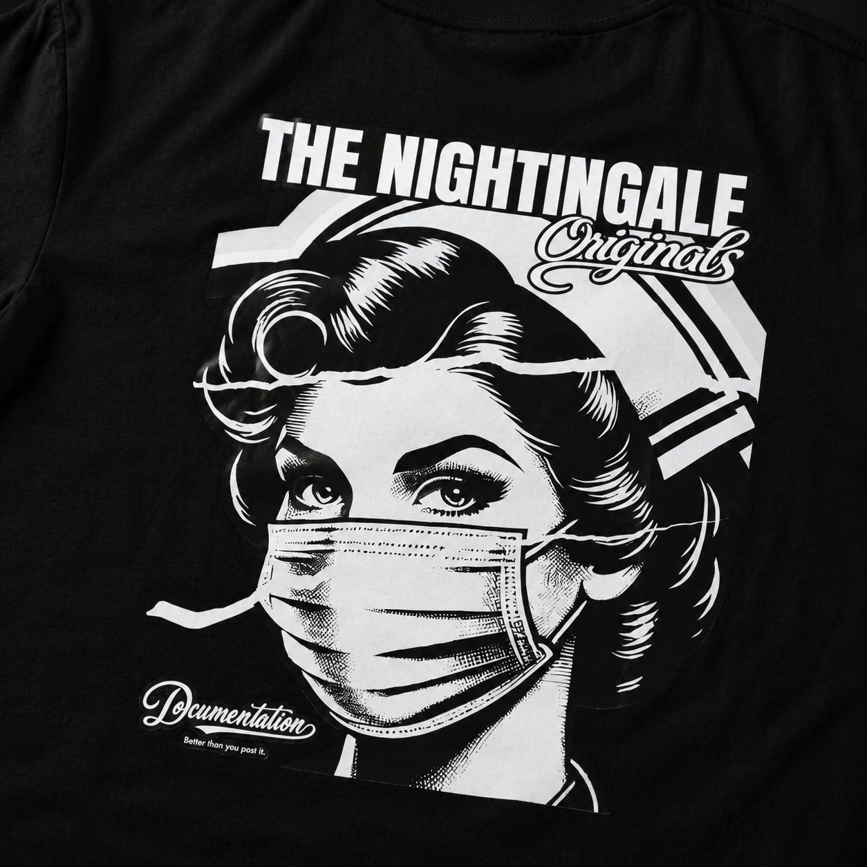 Close-up of the white masked-nurse graphic and Nightingale Originals lettering on a black Sure’t T-shirt.
