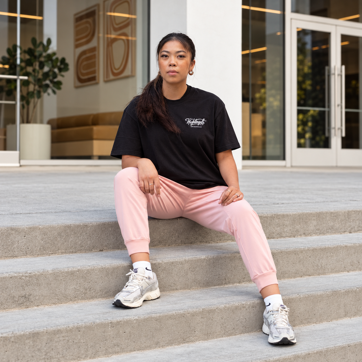 Model in a black Sure’t T-shirt and pink trousers sitting on outdoor concrete steps.
